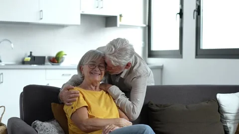 Headshot portrait of smiling elderly 60s husband and wife sit relax on couch hug Stock Footage 237940379