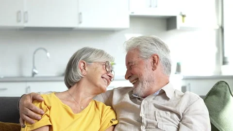 Headshot portrait of smiling elderly 60s husband and wife sit relax on couch hug Stock Footage 237941453