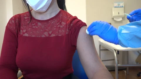 Healtcare worker with protective equipment performs vaccine in female patient Stock Footage 146465089