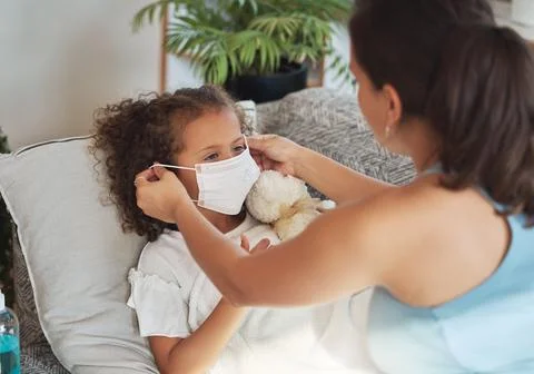 Health care for sick, tired little girl with covid wearing face mask while Stock Photos