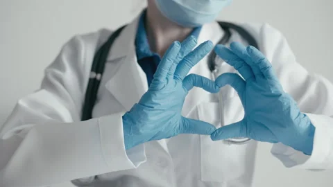 A healthcare worker, symbolizing devotion and safety, forms a heart shape with Stock Footage 277932244