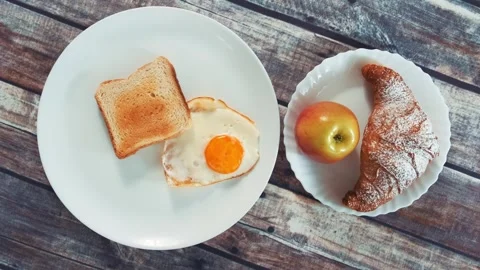 Healthy breakfast featuring fried egg, toast, apple and croissant on table Video stock 340879857