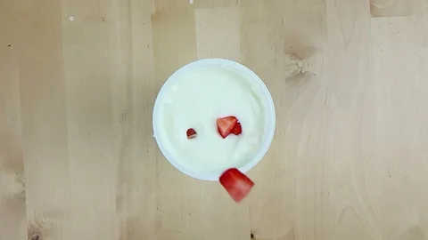 Healthy strawberries falling down on white yogurt in slow motion on wood table Stock Footage 87752621