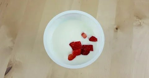 Healthy strawberries falling down on white yogurt on wood table Stock Footage 89540661