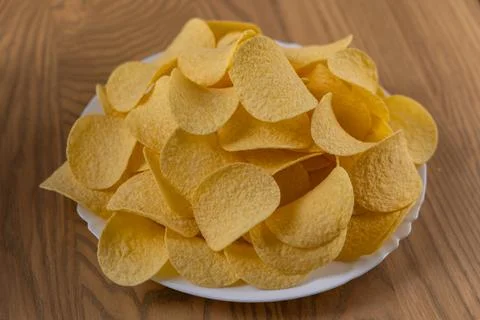 Heap of crispy potato chips on white plate on wooden table Stock Photos