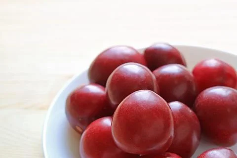 Heap of Fresh Dwarf Gulf Ruby Plum Fruits in a White Plate Foto stock
