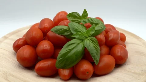 Heap of fresh plump cherry tomatoes rotating on wooden plate on white background Stock Footage 116727723