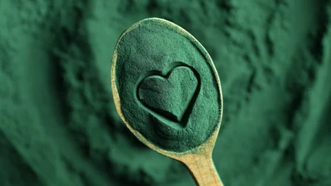 Heap green spirulina algae powder in wooden spoon with heart shape, top view Video stock 333688034
