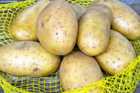 Heap of raw potatos in yellow string bag Stock Photos