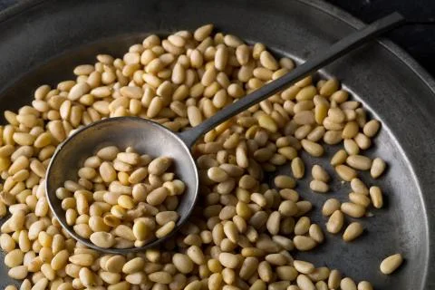 Heap of raw, uncooked pine nuts in metal spoon Foto stock