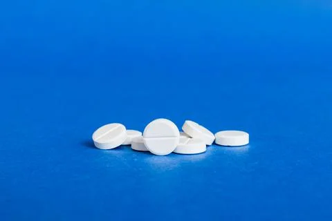 Heap of white pills on colored background. Tablets scattered on a table. Pile Stock Photos