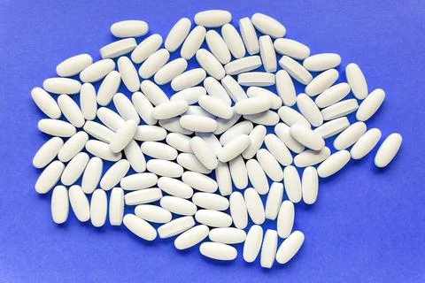 Heap of white tablets on blue background. Stock Photos