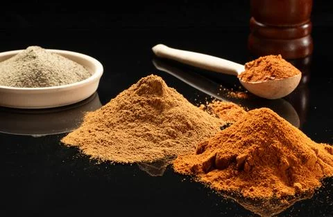 Heaps of different spices on a mirror black table lit by the morning sun Stock Photos