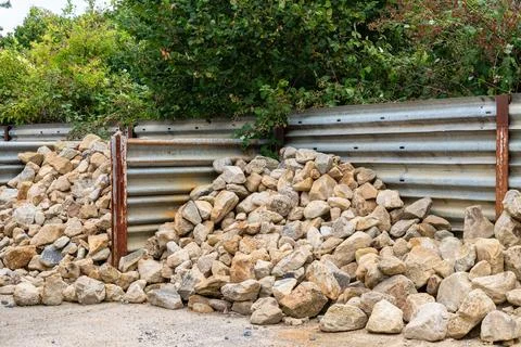 Heaps of grey-brown cobblestone piled near a metal fence. Stock Photos