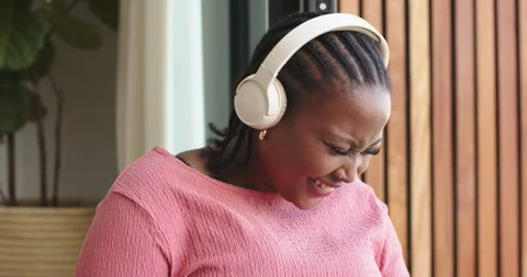 Hearing amusing audio, African American woman with headphones smiling then Stock Footage 337624280