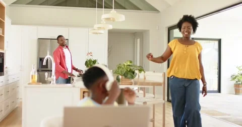 Hearing footsteps Black boy working on laptop at table while mother leaning with Stock Footage 344333432