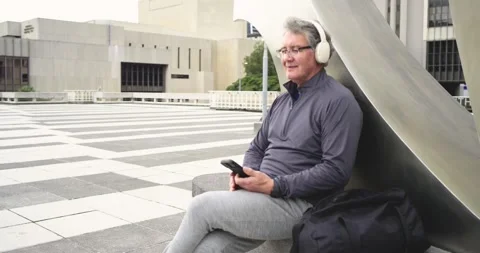 Hearing noise, man with headphones tapping smartphone, glancing up smiling on Stock Footage 342392099
