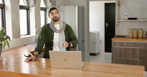 Hearing off-screen cue, Indian man lifting mug, sipping coffee on kitchen island Stock Footage 342595824