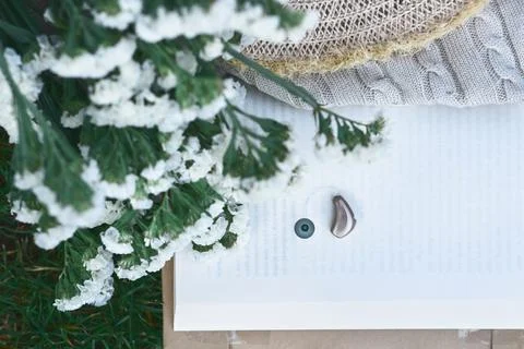 Hearing solutions, concept. Open book reveals a hearing aid beside white fl.. Stock Photos