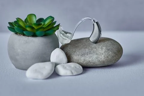 Hearing solutions, concept. Sleek hearing aid on grey stone in minimalist sty Stock Photos