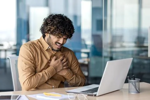 Heart attack and panic attack in the workplace. Young Indian man suffering from Foto stock