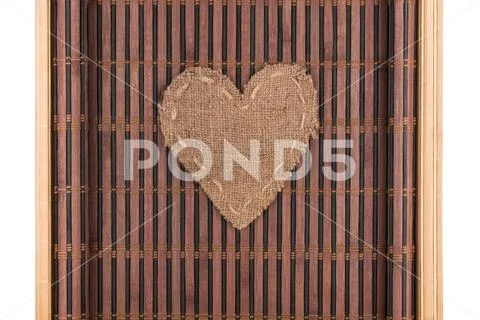 Heart made of burlap lies on a bamboo mat with curved edges. Stock Photos