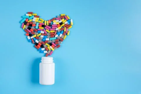 The heart is made up of colored tablets in the white bottle on a blue backgro Stock Photos