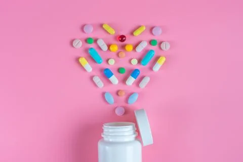The heart is made up of colored tablets in the white bottle on a pink backgro Stock Photos