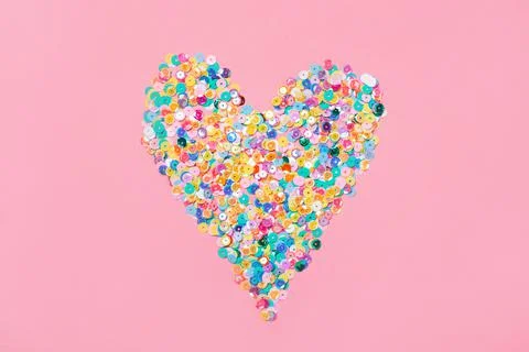 Heart made of multicolored sequins confetti on pink background. Flat festive Stock Photos