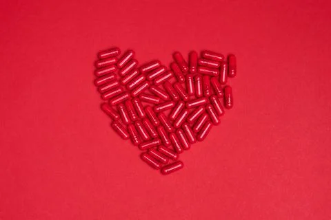 Heart made of red capsule pills vitamin on a colorful background. Health supp Stock Photos