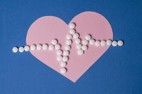 Heart pulse is lined with small white pills on a paper pink heart background. Stock Photos