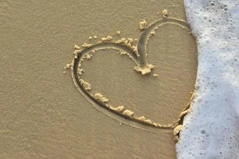 Heart on a sand of beach with wave on background Stock Photos