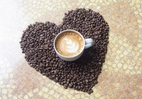 Heart shape created with roasted coffee grains and a cup of coffee in the mid Stock Photos