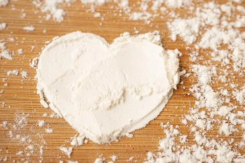 Heart shape created with white flour on a wooden surface, surrounded by sca.. Stock-Fotos