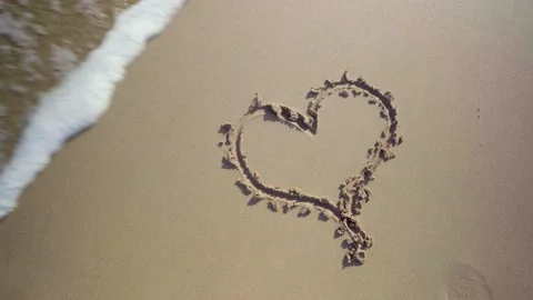 Heart shape drawing in the sand at the beach is getting washed away by a Stock Footage 147904705
