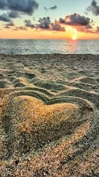 Heart shape drawn in sand during sunset at the beach by the ocean with wave.. Stock Photos