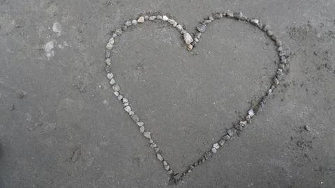 Heart shape drawn in small gray stones on textured concrete surface, sweet. Stock Photos
