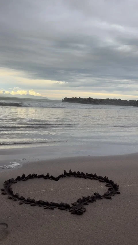 Heart shape drawn in wet sand on empty beach at calm ocean shoreline Stock Footage 326511476