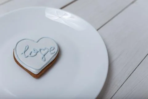 Heart shape gingerbread cookie on white plate standing on white wooden table Stock-Fotos