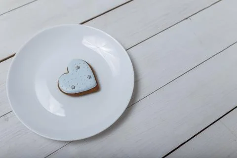 Heart shape gingerbread cookie on white plate standing on white wooden table Stock-Fotos