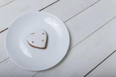 Heart shape gingerbread cookie on white plate standing on white wooden table Stock Photos
