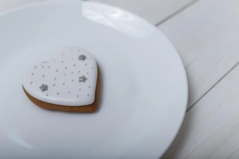 Heart shape gingerbread cookie on white plate standing on white wooden table Stock-Fotos