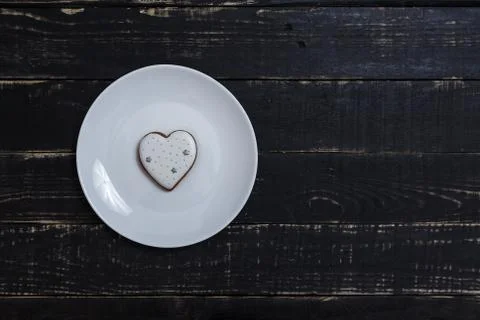 Heart shape gingerbread cookie on white plate standing on black wooden table Stock-Fotos