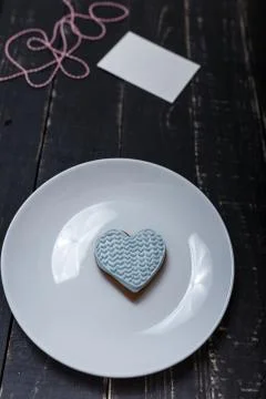 Heart shape gingerbread cookie on white plate standing on black wooden table Stock Photos