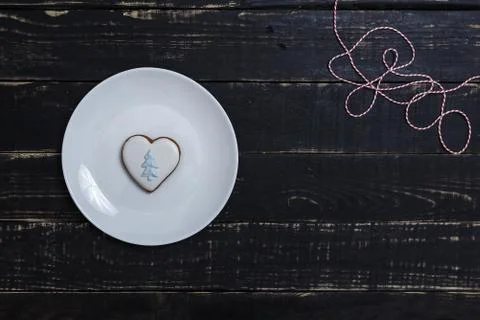 Heart shape gingerbread cookie on white plate standing on black wooden table Stock Photos