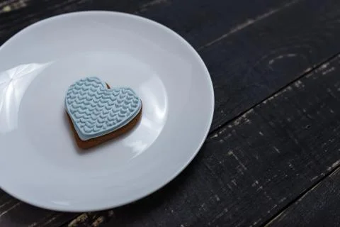 Heart shape gingerbread cookie on white plate standing on black wooden table Stock Photos