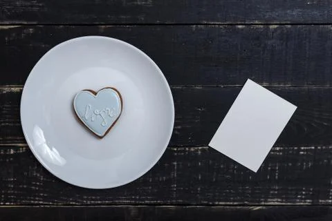 Heart shape gingerbread cookie on white plate standing on black wooden table Stock Photos