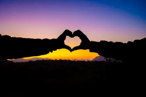 Heart shape by hands in silhouette while watching the sunset Stock Photos