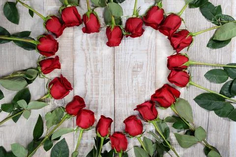 Heart shape lined with red roses on a light wooden texture background. Love s Stock Photos