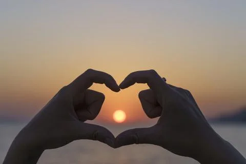 Heart shape made of hands against the sunset sun over the sea Stock Photos